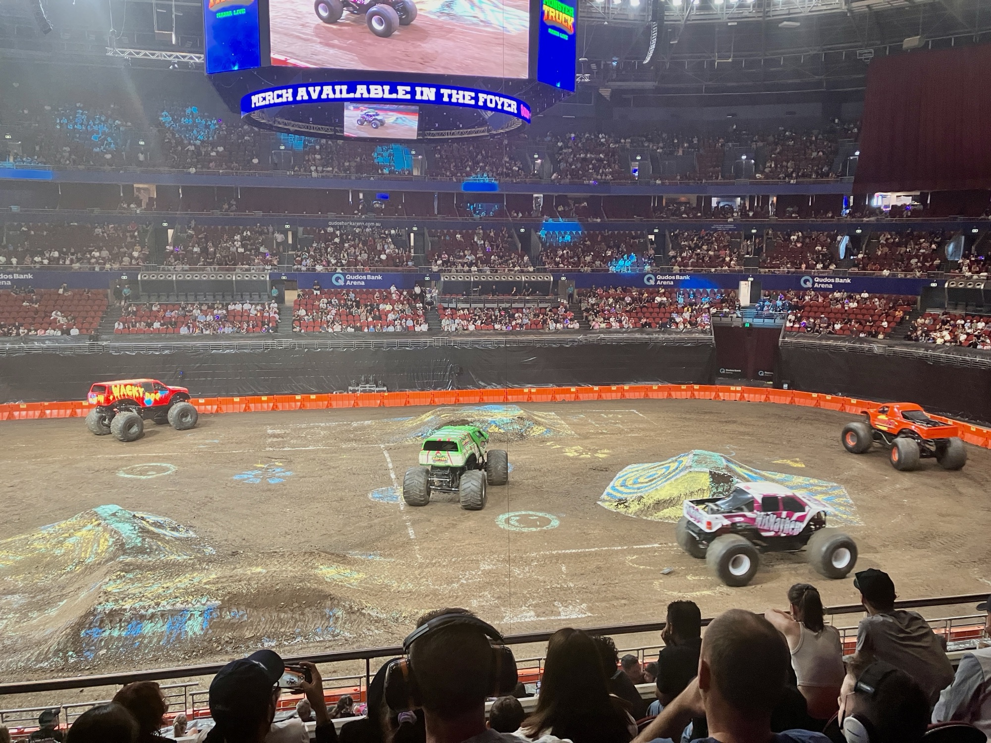 A parade of monster trucks dicking around in an arena
